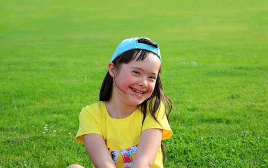 Young girl with down syndrome sitting in green grass. Donate to your Lansing community.